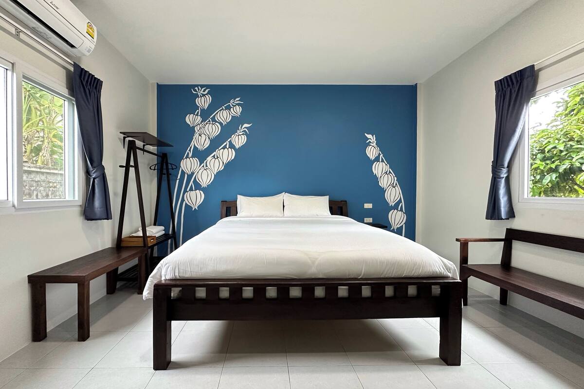 Un dormitorio con una cama, dos bancos, una lámpara de pie y una pared azul con un diseño de planta.
