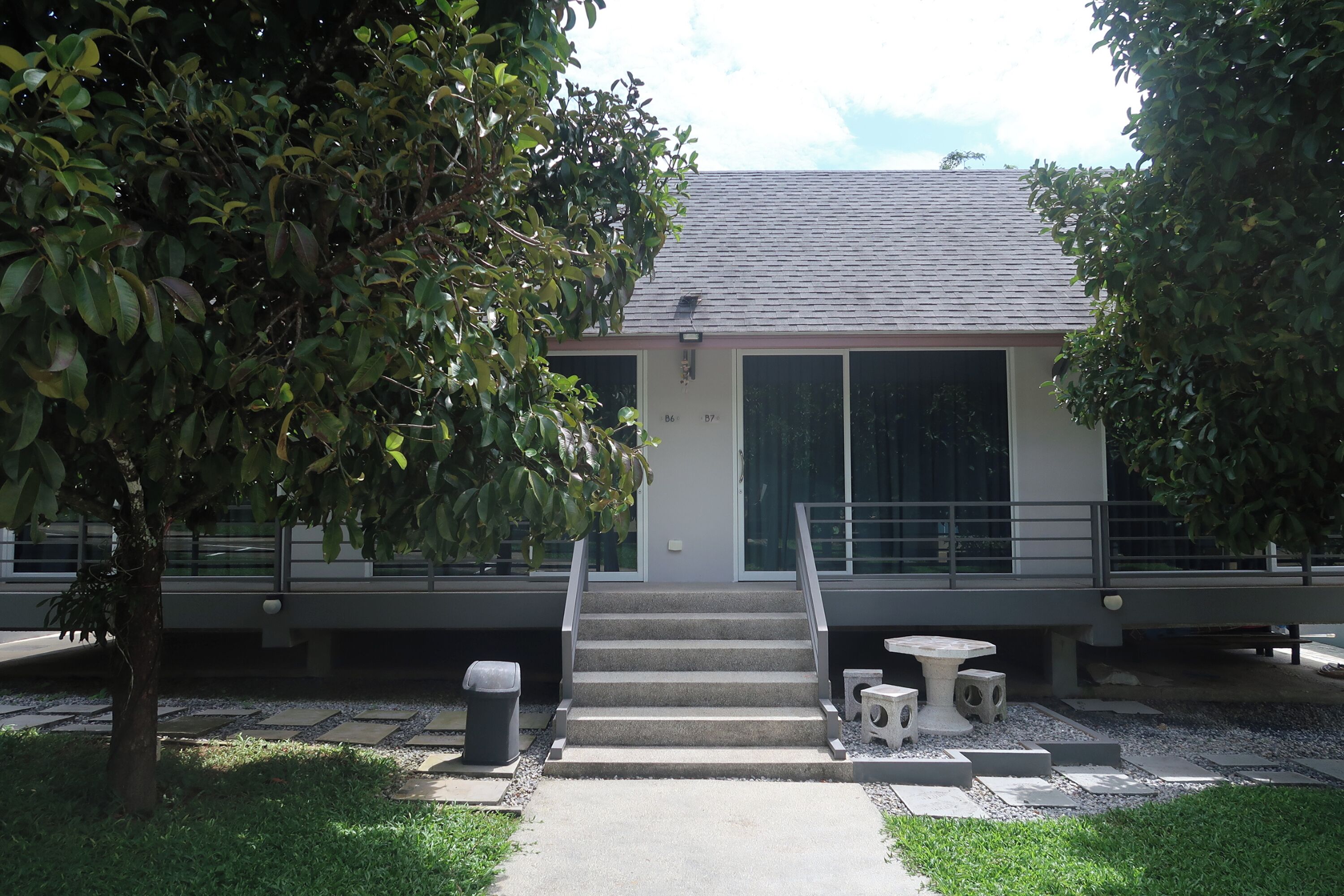A modern building with a grey roof, a staircase leading to a door, and a small outdoor seating area with a table and chairs.