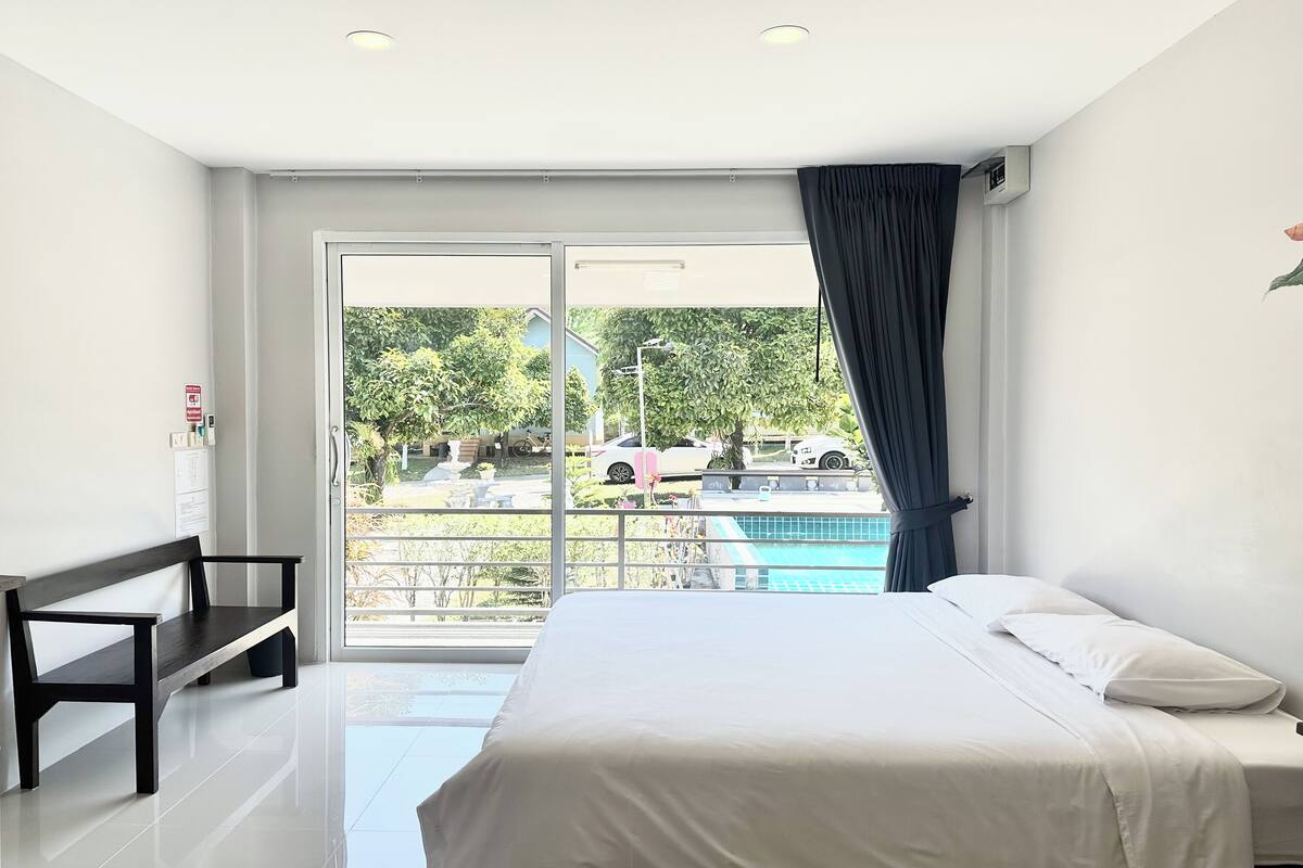 Habitación de hotel con cama, una banca, vista a una piscina y puerta al exterior.