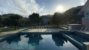A swimming pool with clear blue tiles, surrounded by a paved area and trees. - Be Leaf Resort (Thep Krasattri)
