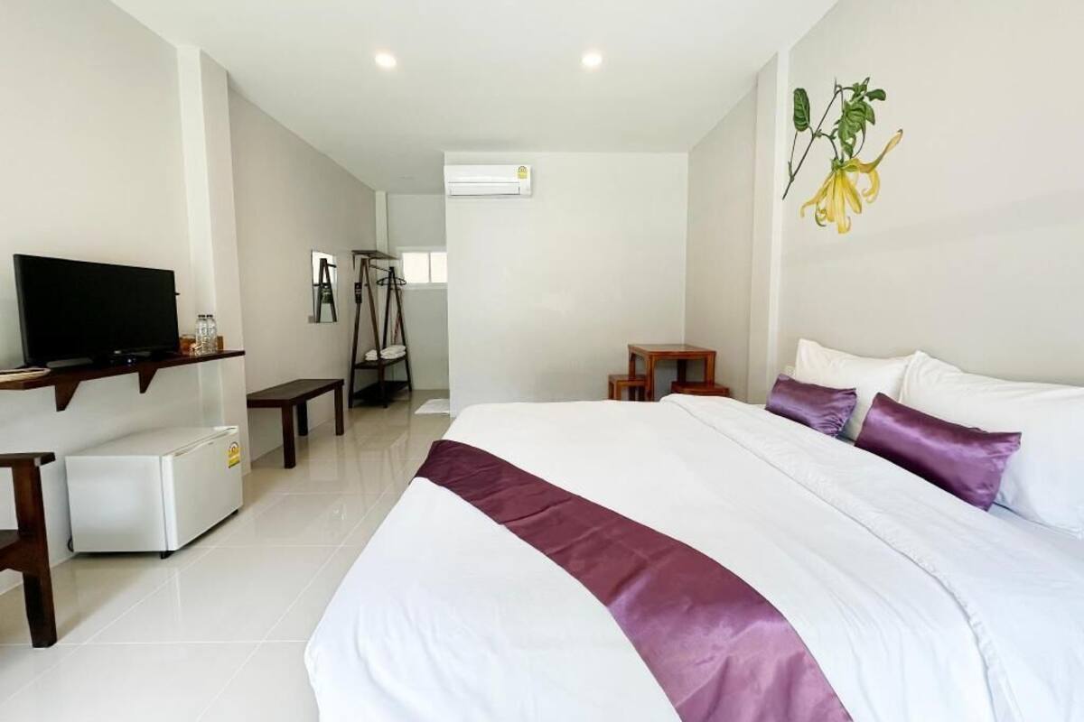Habitación de hotel con cama, televisor, refrigerador pequeño, escritorio y espejo.