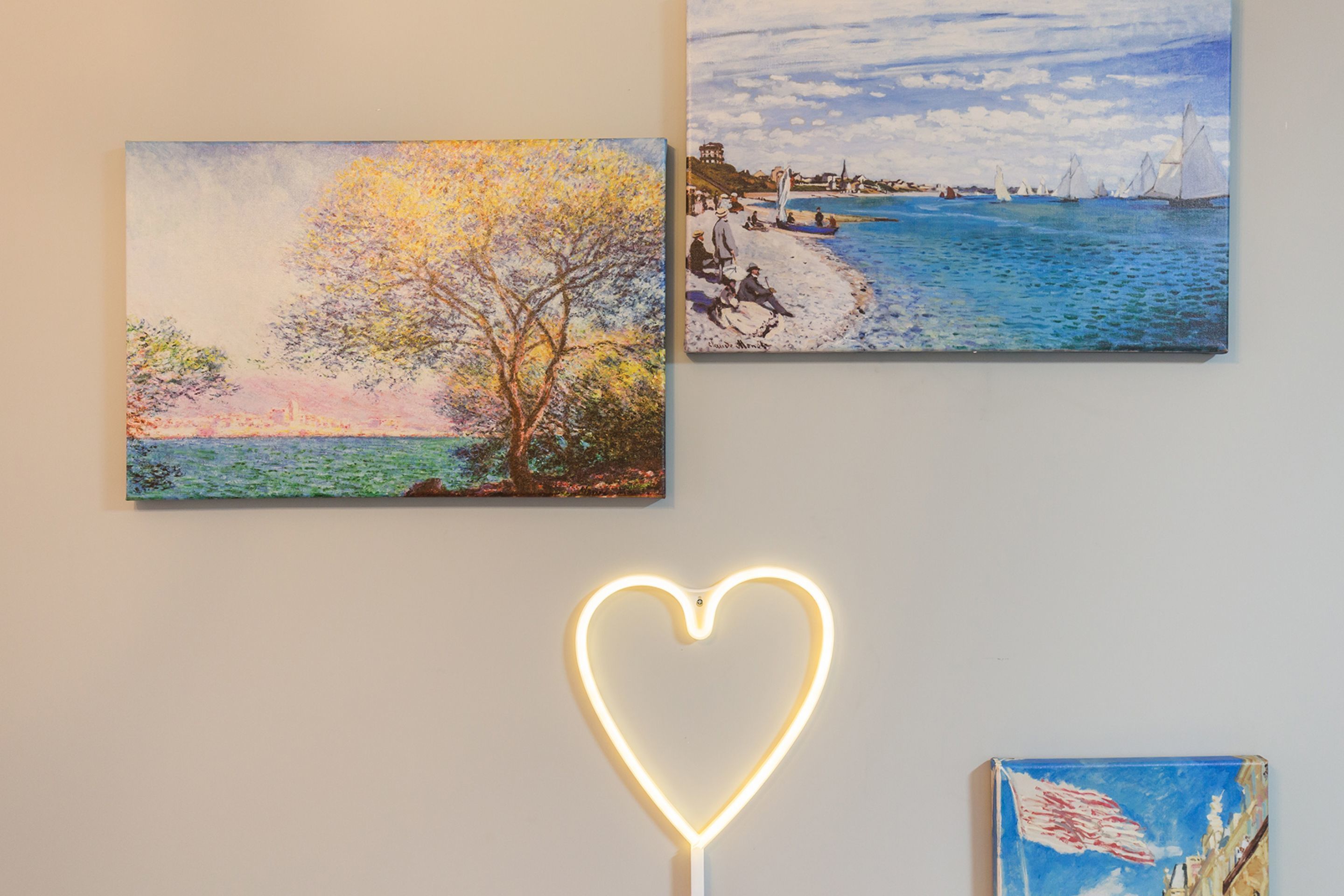 Two paintings and a neon heart sign on a wall.