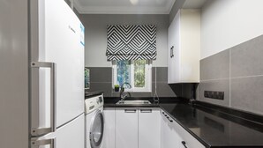 A compact kitchen with a washing machine, a sink, and a window with a geometric valance.
