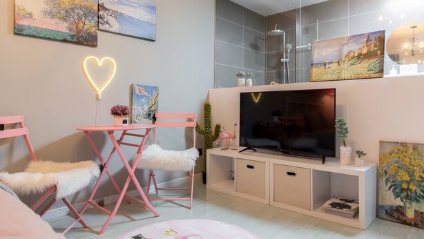 A modern living room with a TV, pink furniture, and artwork on the walls.