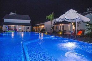 A swimming pool with a unicorn float, a covered seating area, and a house in the background.