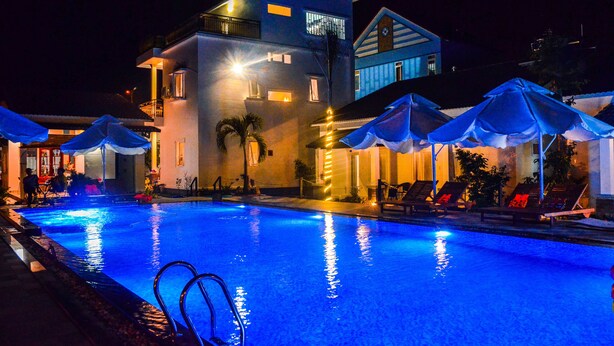 Una piscina con sillas de descanso y sombrillas, rodeada por un edificio con varios pisos y balcones.