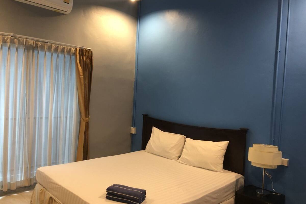A hotel room with a bed, curtains, a nightstand with a lamp, and an air conditioning unit.