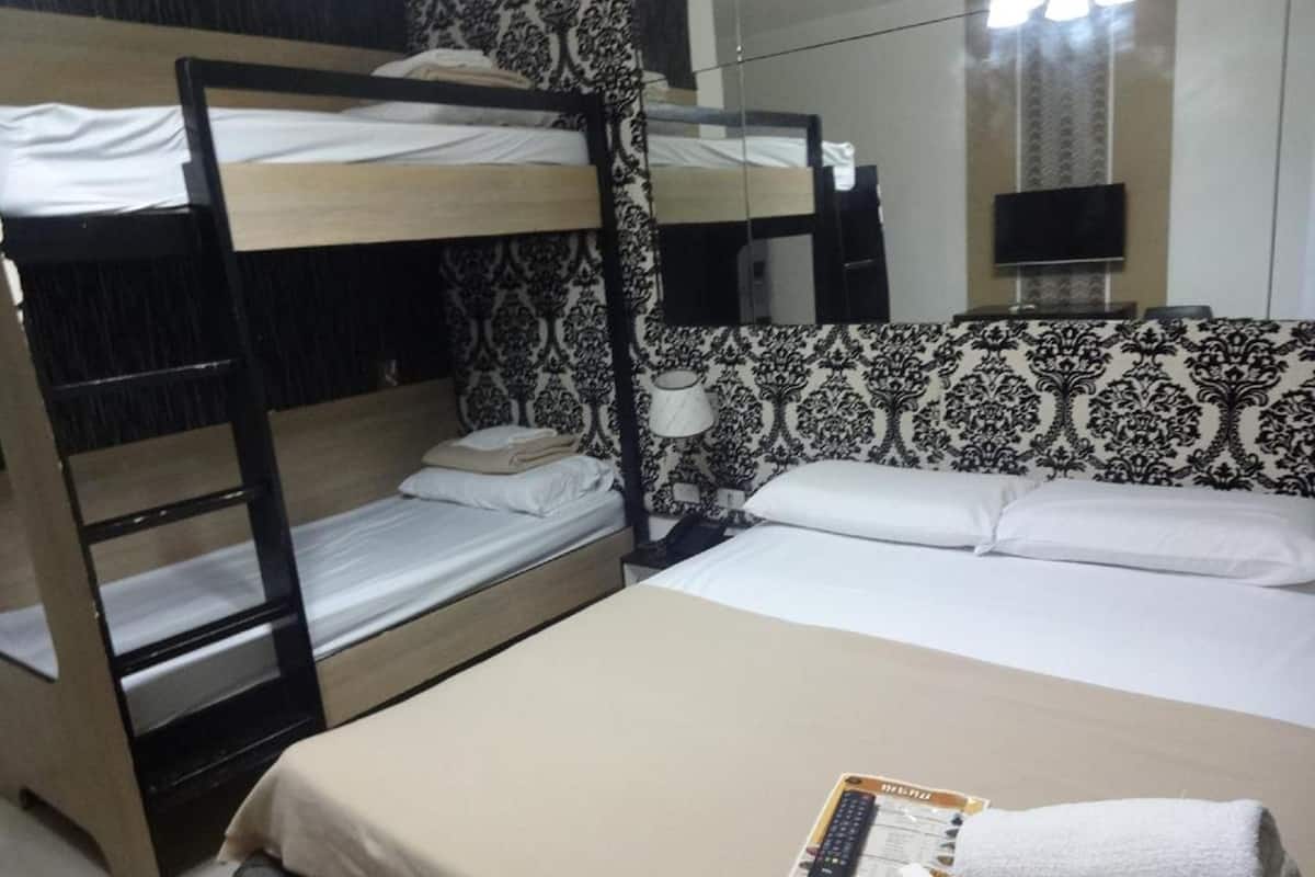 A hotel room with bunk beds, a flat bed, a mirror, a TV, and a menu on the bed.