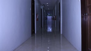 A long, narrow hallway with white walls and a shiny tiled floor. There are doors on both sides and fire extinguishers mounted on the walls. - Heilee's Guest House (General Santos)
