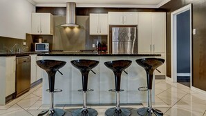 A modern kitchen with four bar stools, stainless steel appliances, and a central island. - Hollywood Tree House (Burnside)
