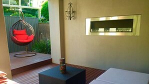 A modern outdoor seating area with a hanging chair, a small table with a can, and a framed picture on the wall. - Hollywood Tree House (Burnside)