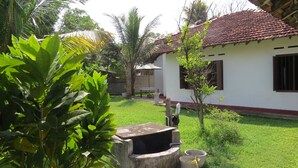 A white building with a red-tiled roof, surrounded by lush greenery and a small tree. - Mendis Cottage (Ahangama)