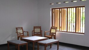 A room with a table and four chairs, a window with vertical blinds, and a concrete floor. - Mendis Cottage (Ahangama)