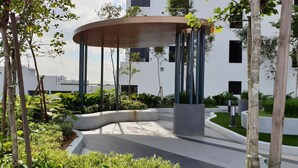 Un espace extérieur moderne doté d’un coin salon aux lignes courbes, entouré de verdure et bordé d’un bâtiment aux nombreuses fenêtres.