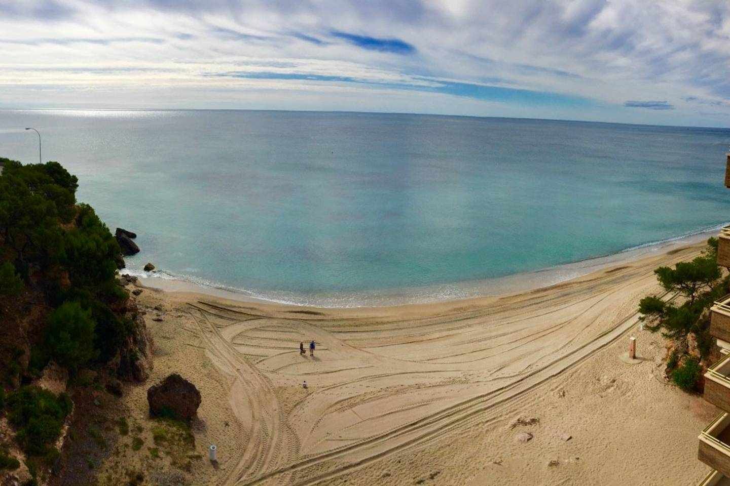 Una playa con vista despejada al océano, un sendero arenoso que lleva al agua y un edificio a la derecha.