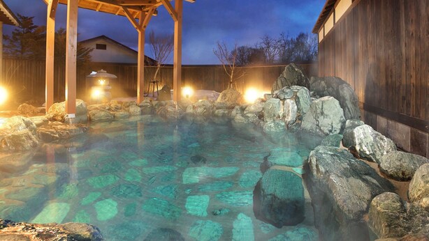 Un área de aguas termales con agua cristalina, rocas y construcciones de madera.