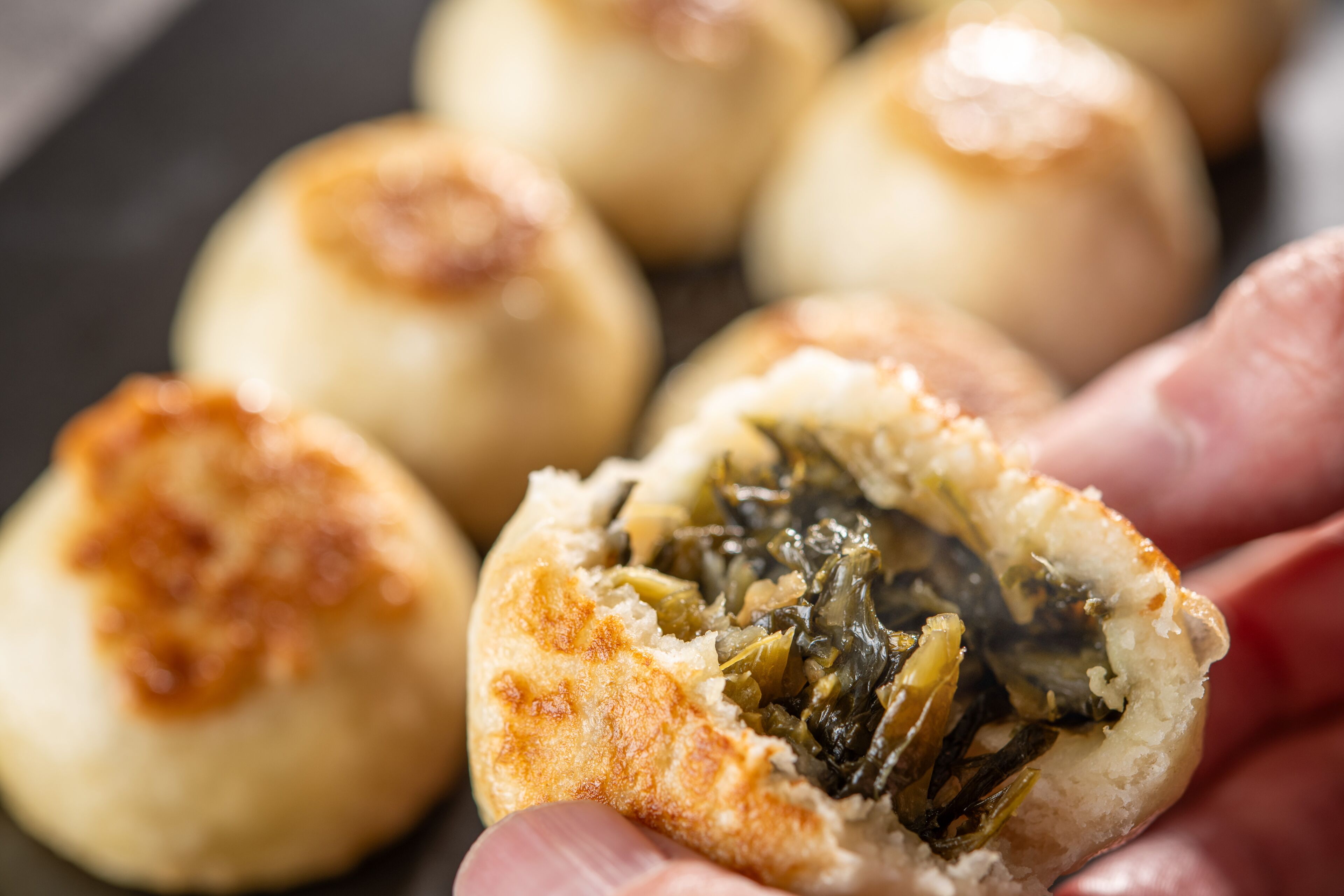 Nahaufnahme einer Hand, die einen gedämpften Brötchen mit deutlich sichtbarer Füllung aus Gemüse hält.