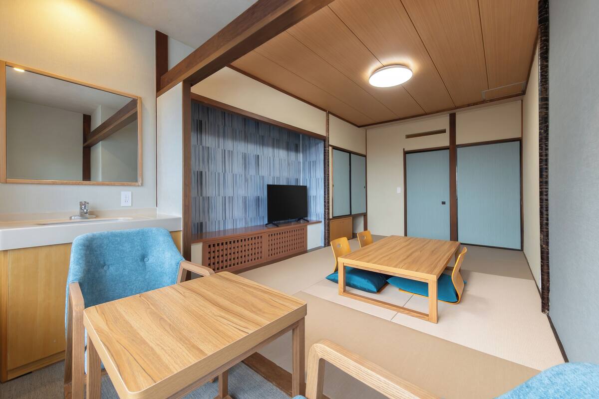 Une pièce comprenant une table à manger en bois, des chaises bleues, un téléviseur posé sur un meuble en bois, un miroir et des portes coulissantes.
