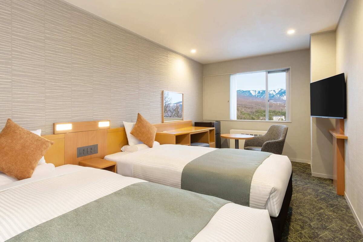 Une chambre d’hôtel avec deux lits, un bureau, une chaise, une télévision et une fenêtre donnant sur la montagne.