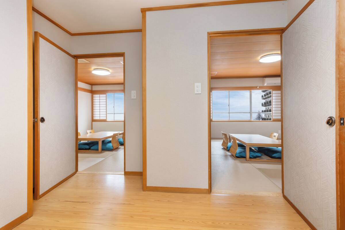Une pièce de style japonais traditionnel, avec un sol recouvert de tatamis, des portes coulissantes et une vue sur le paysage urbain par une fenêtre.
