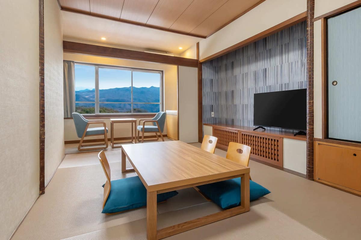 Una habitación con una mesa de comedor de madera, sillas, un televisor y vistas a montañas a través de amplias ventanas.