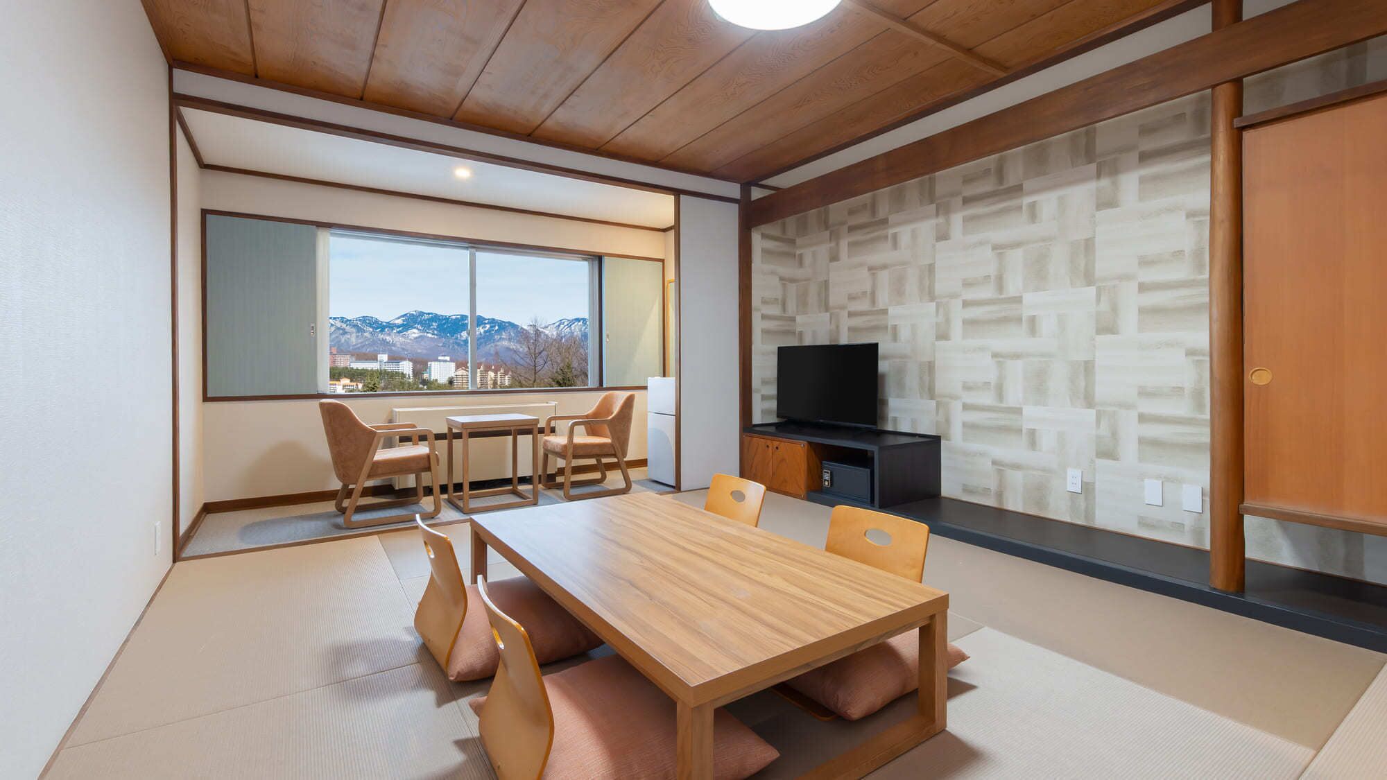 A modern living room with a wooden dining table, chairs, a television, and a view of mountains through large windows.