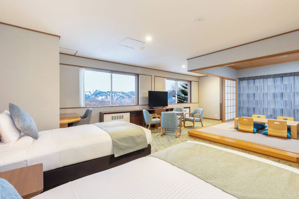 Une chambre d’hôtel avec deux lits, un bureau, une télévision et un coin salon comprenant des chaises et une table.