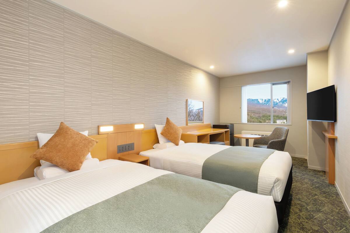 Une chambre d’hôtel avec deux lits, un bureau, une chaise, une télévision et une fenêtre donnant sur la montagne.