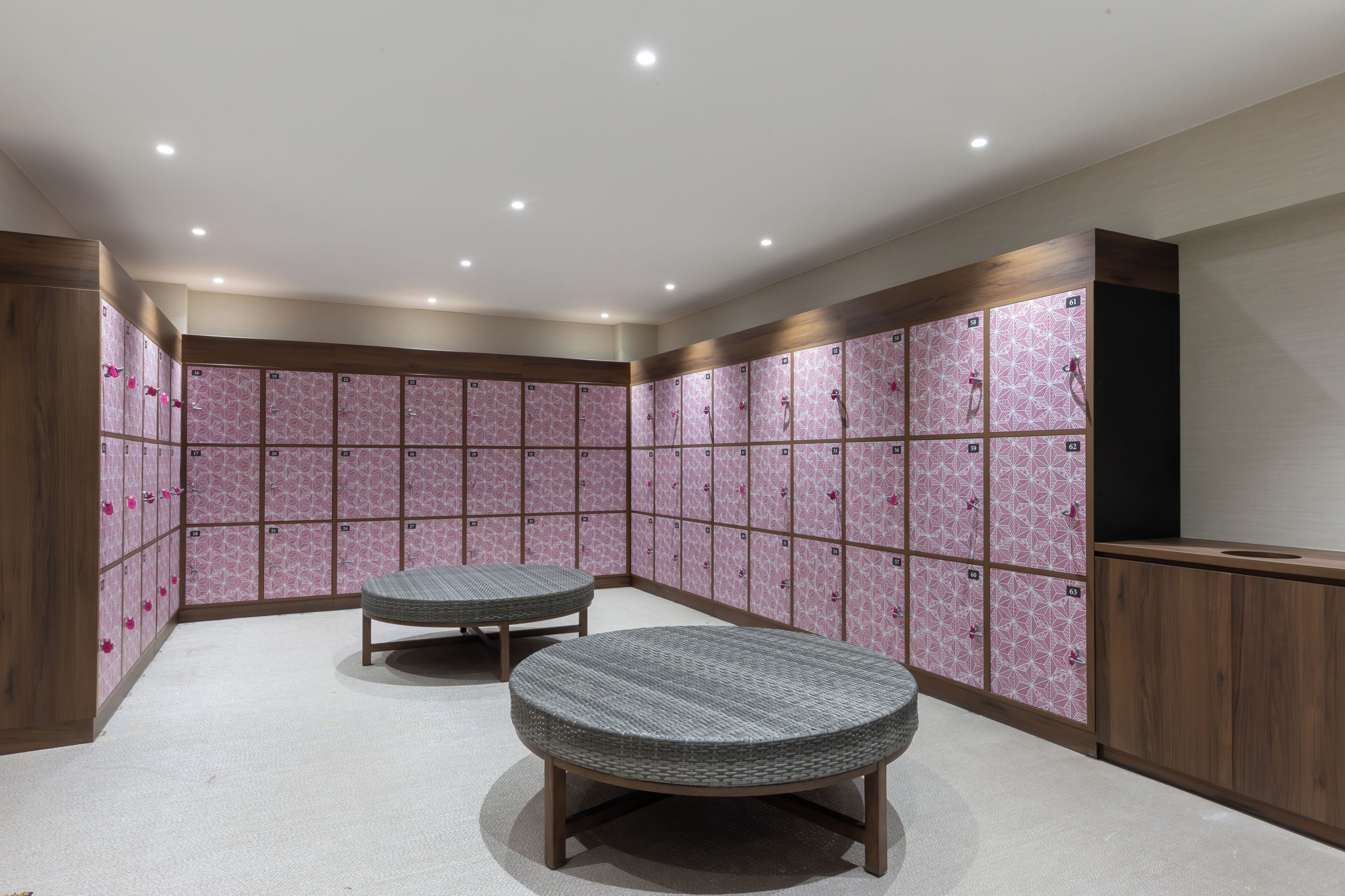 A locker room with multiple lockers, two round tables, and wooden cabinets.