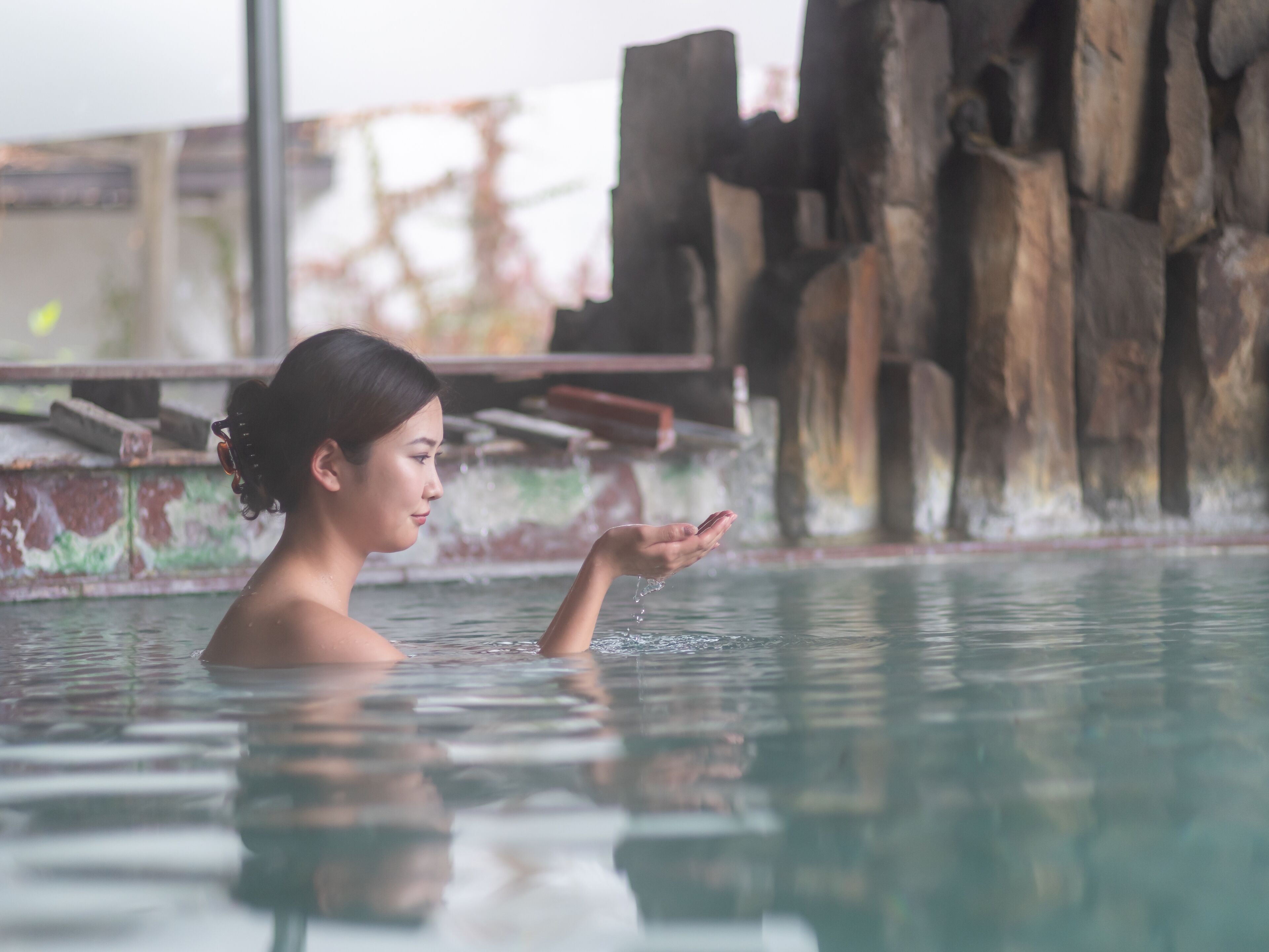 Una persona en una piscina, con una estructura de madera al fondo.