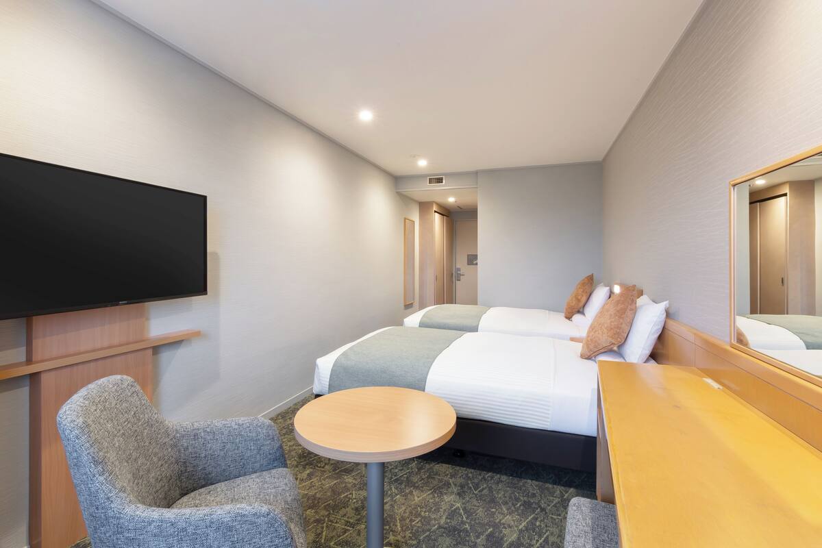 Une chambre d’hôtel équipée d’un téléviseur à écran plat, de deux lits, d’une petite table ronde et d’un bureau en bois.