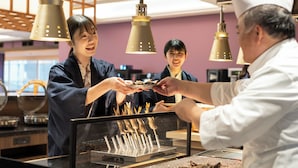Interior de un restaurante con mostrador, luces colgantes y una vitrina con brochetas.
