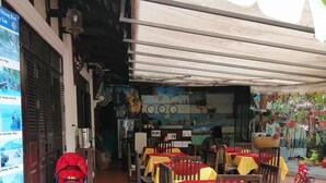 Un espace extérieur aménagé avec des tables recouvertes de nappes jaunes et rouges, des chaises en bois et des plantes en pot.