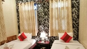 Une chambre d’hôtel avec deux lits, chacun doté de draps blancs et d’oreillers rouges, une table de chevet avec une lampe et un mur décoré d’un motif marbré.