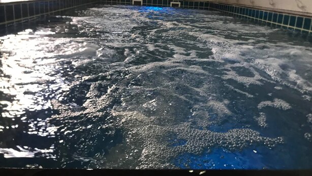 Un bain à remous avec de l’eau bouillonnante, entouré d’une zone carrelée dont les murs présentent un motif évoquant le marbre.