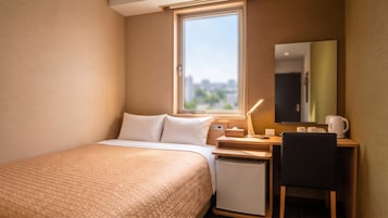 Habitación de hotel con cama, escritorio, silla, refrigerador pequeño, mesita de noche con lámpara y ventana con vista a la ciudad.