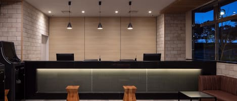 Zona de recepción con mostrador, taburetes de madera, sofá e iluminación colgante.