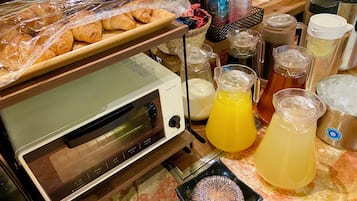 A kitchen counter with a toaster oven, plastic-wrapped pastries, and various beverage containers.