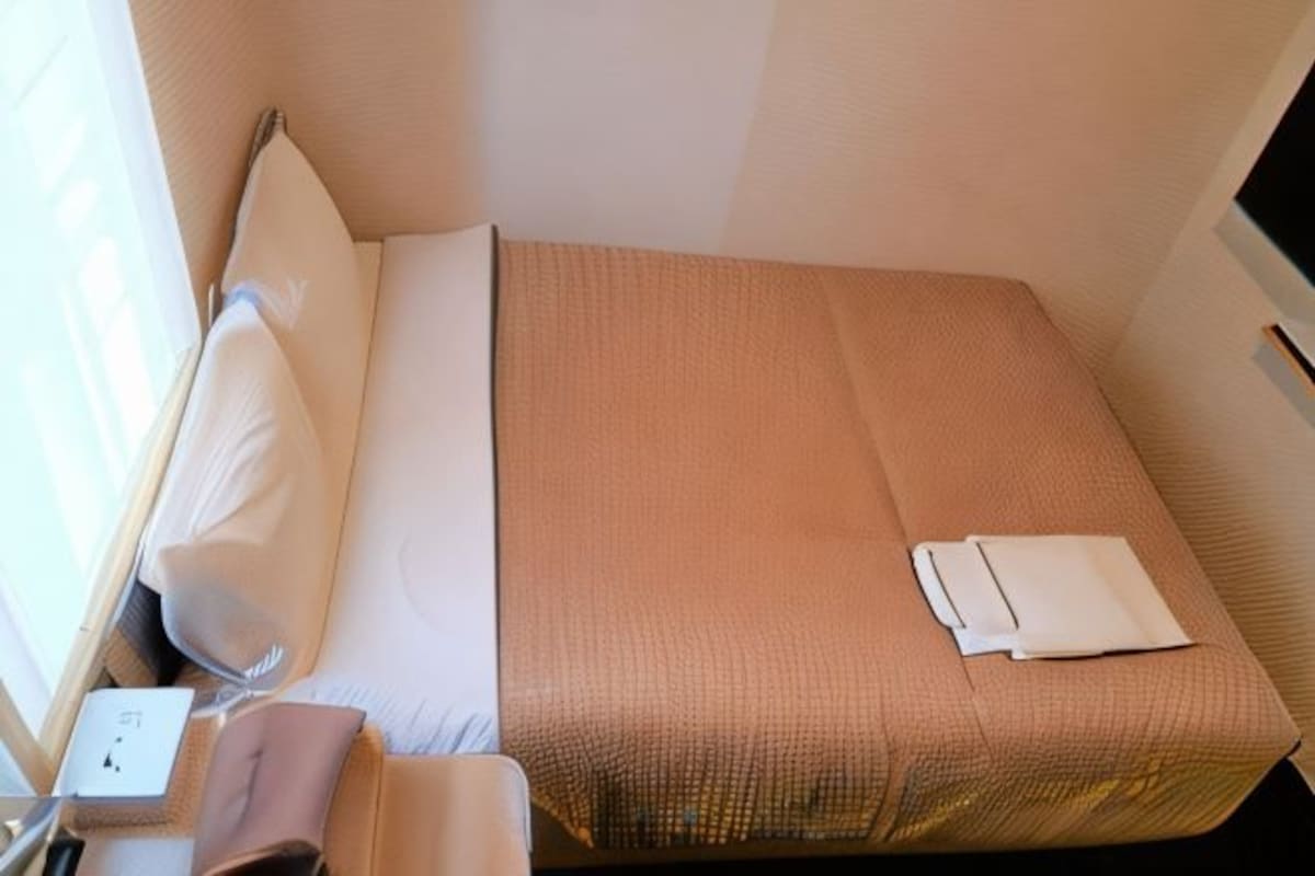 A single bed with a beige bedspread, a pillow, and a folded white towel.