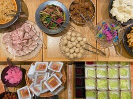 Diversos tipos de alimentos, como carne cortada, verduras y postres, dispuestos sobre una mesa de madera.