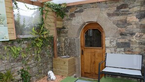 A stone-walled room with a wooden door, a bench, and potted plants. - Gîte 3 pers. between Land and North Brittany Sea (Tréduder)