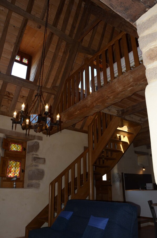 A wooden staircase with a chandelier, a stone wall, and a window with stained glass.