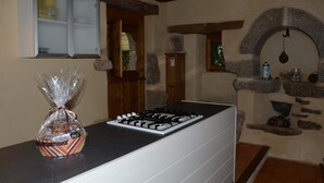 A kitchen with a gas stove, a cabinet with glass doors, and a stone wall with a fireplace. - Gîte 3 pers. between Land and North Brittany Sea (Tréduder)