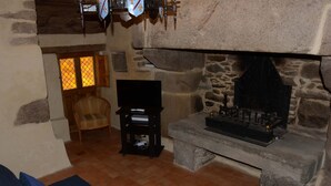 A stone fireplace with a mantel, a wooden chair, and a small table with a television. - Gîte 3 pers. between Land and North Brittany Sea (Tréduder)