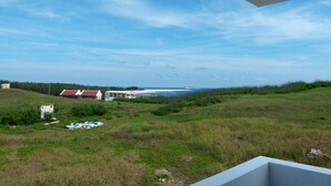 A view from a balcony overlooking a grassy landscape with a beach and a few buildings in the distance.
