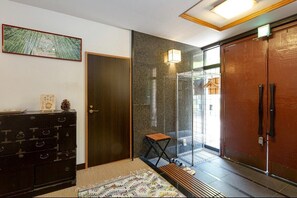 A room with a dark wooden wardrobe, a small wooden stool, a patterned rug, and a wall-mounted light fixture. - Cottage EMI (Kyoto)