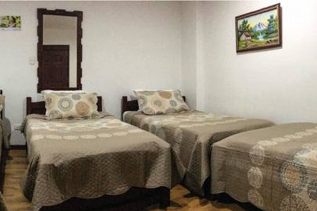 A room with two single beds, a wooden door, a framed picture on the wall, and a small table with a chair.