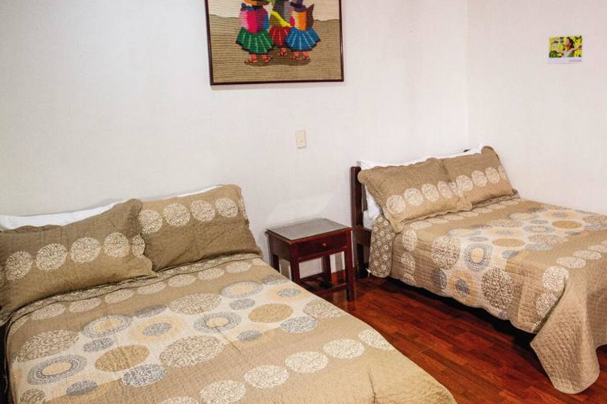 A room with two beds, each with a patterned bedspread, a small wooden nightstand, and a framed picture on the wall.