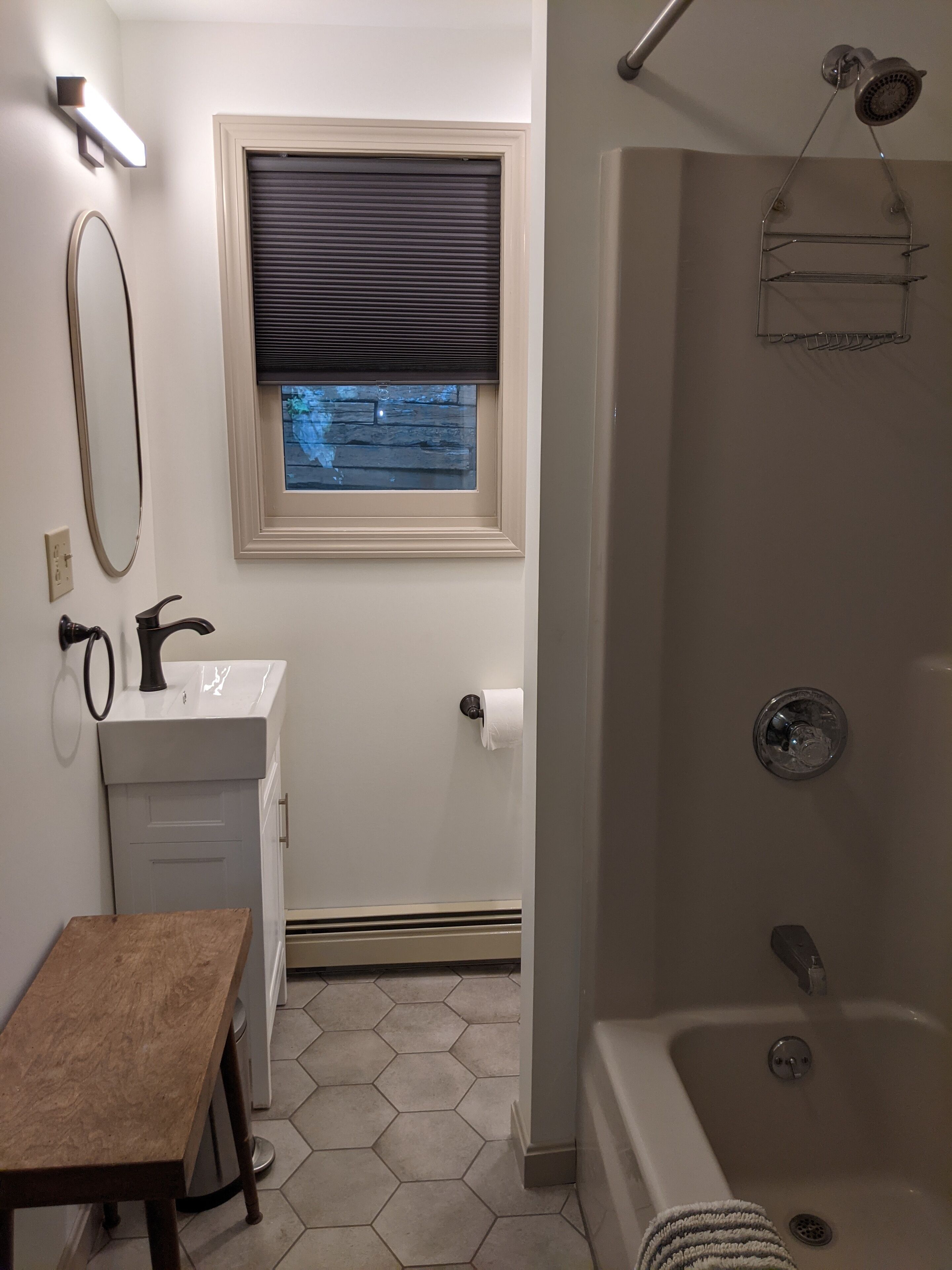 A bathroom with a bathtub, a toilet, a sink, a window with blinds, and a towel rack.