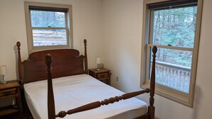 Una cama con dosel, un cabecero de madera, dos mesitas de noche con lámparas y amplios ventanales con vistas a un área boscosa.
